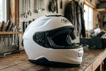 Casque moto Shoei GT Air 2 blanc posé sur un établi en bois dans un atelier moto, vue trois quarts montrant les détails de ventilation et le visière solaire intégrée