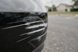 Rayure profonde sur un pare-chocs noir révélant le plastique blanc en dessous, visible sur une voiture garée